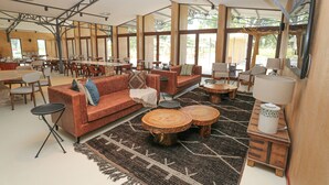 A spacious indoor area with a large sofa, multiple tables, and chairs arranged for dining and relaxation. - Mumba Lodge by Flow (Cuvango)