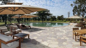 A poolside area with stone flooring, wooden furniture, and large umbrellas. - Mumba Lodge by Flow (Cuvango)