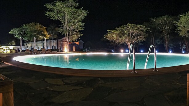 A nighttime swimming pool with a stone deck, metal pool ladder, and surrounding trees. - Mumba Lodge by Flow (Cuvango)