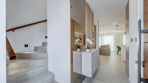 Un interno moderno con una scala, un banco reception minimalista e una zona living con un divano e una poltrona verde.