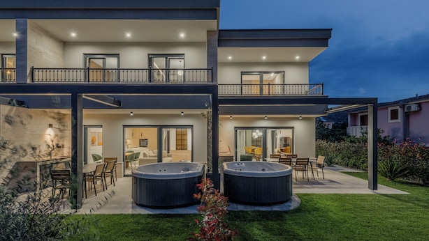Una moderna casa a due piani con patio coperto, vasche idromassaggio e un prato curato.