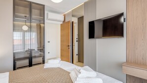 Una camera d'albergo moderna con un letto grande, una TV fissata al muro e una porta scorrevole in vetro che dà su un balcone.