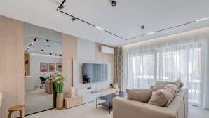 Un soggiorno moderno con un divano, un tavolino, una TV a parete e un'area pranzo sullo sfondo.