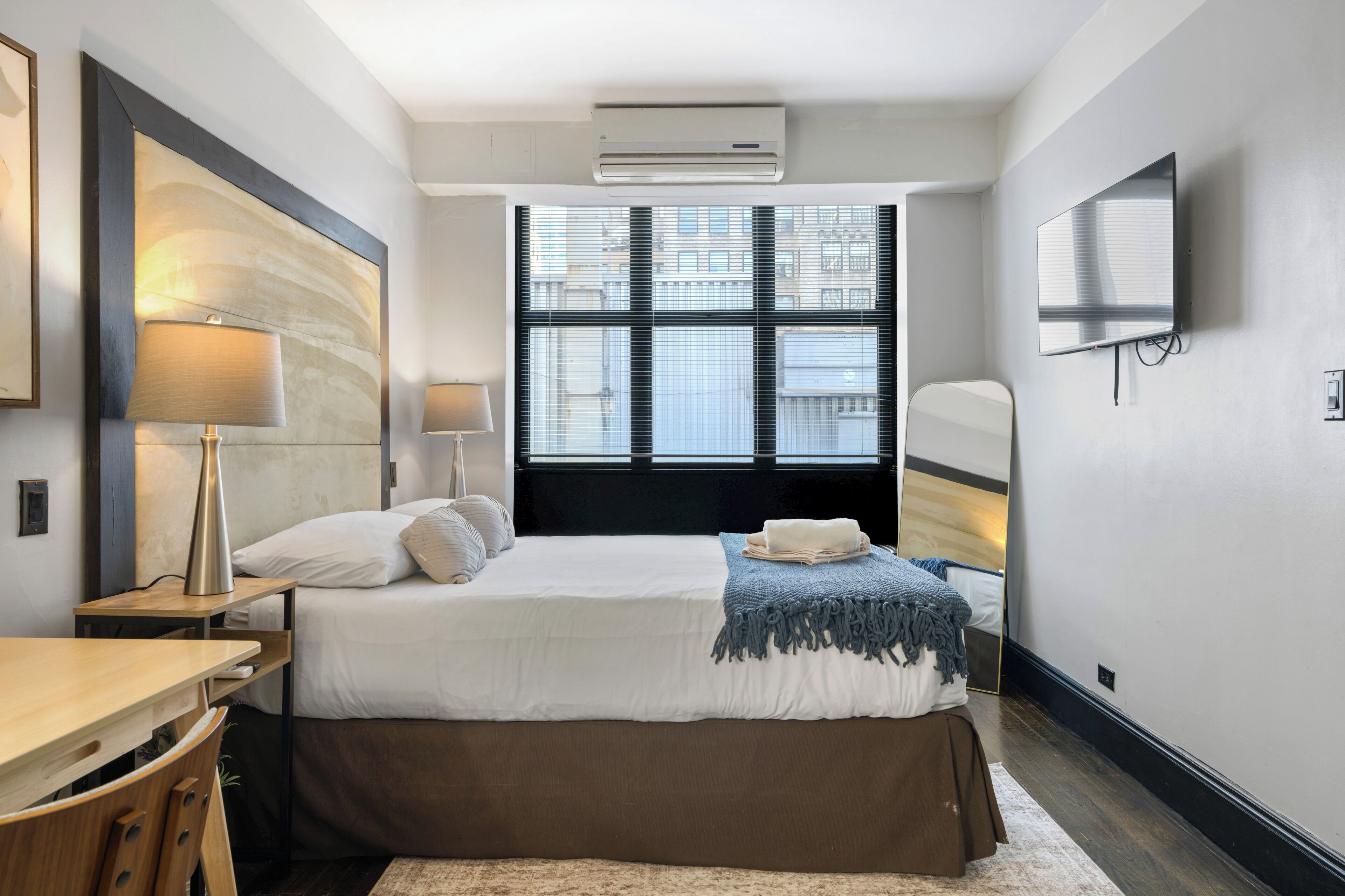 Une chambre d’hôtel avec un grand lit, un bureau, une chaise, une télévision et une fenêtre avec des stores.