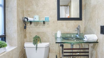 A bathroom with a toilet, glass sink, and a mirror above the sink.