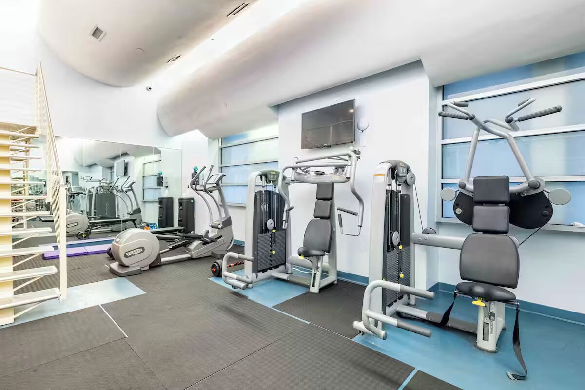 Een sportschool met trainingsapparatuur, een spiegel en een televisie aan de muur.