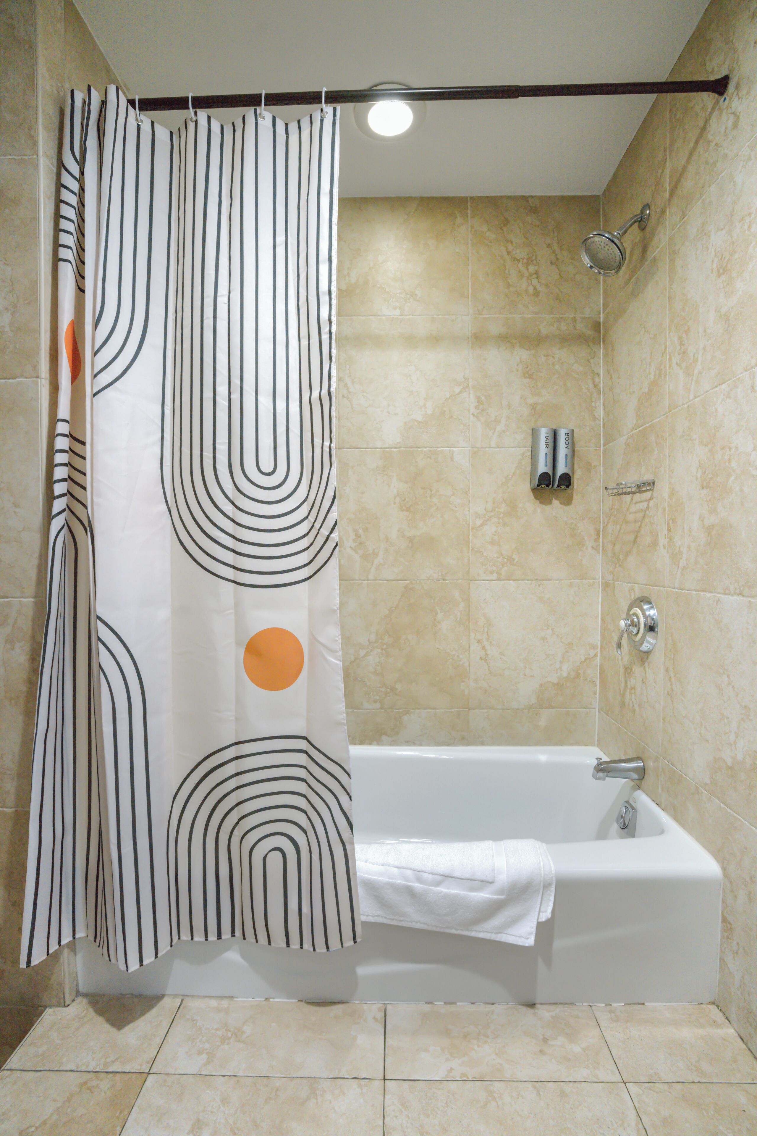 Une salle de bain avec une baignoire, un rideau de douche à motifs géométriques et des murs recouverts de carreaux beiges.