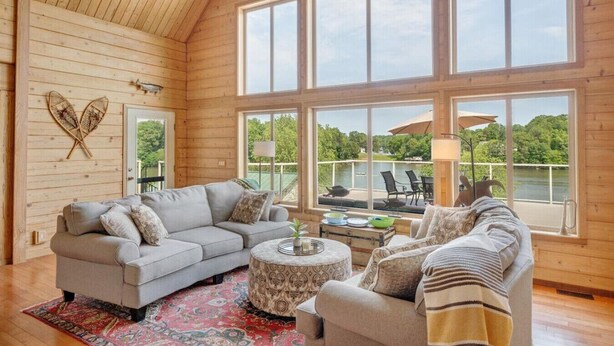L’intérieur d’un chalet chaleureux, avec une grande fenêtre donnant sur un lac et la verdure environnante.