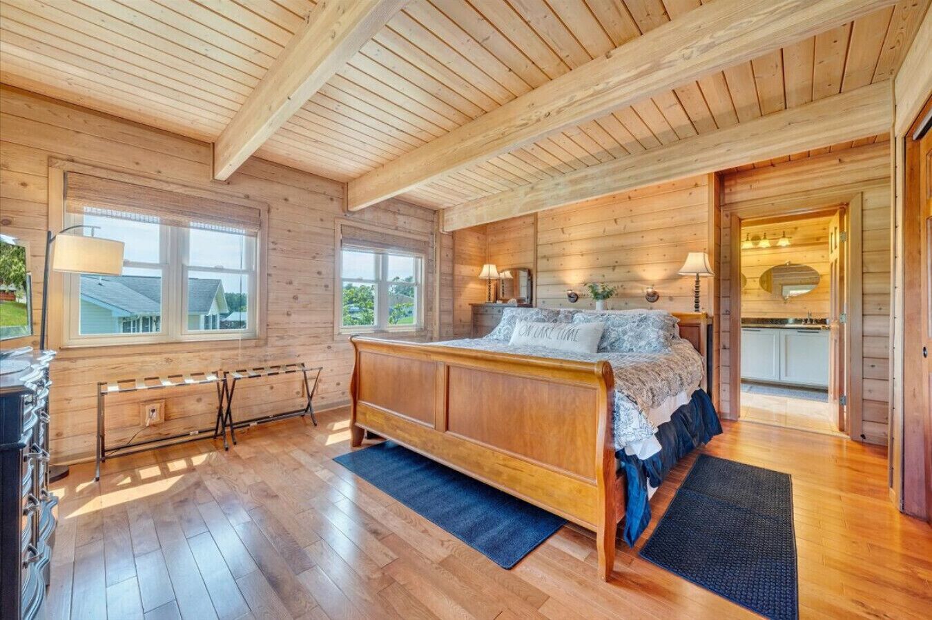 A wooden cabin bedroom with a bed, windows, and a view of the outside.