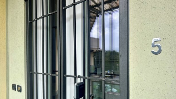 Ein Gebäudeeingang mit einem Metallgitter, einer Glastür und der Zahl 5 an der Wand.