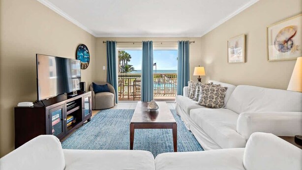 A hotel room with a living area featuring a TV, sofa, and a view of the ocean through large windows.