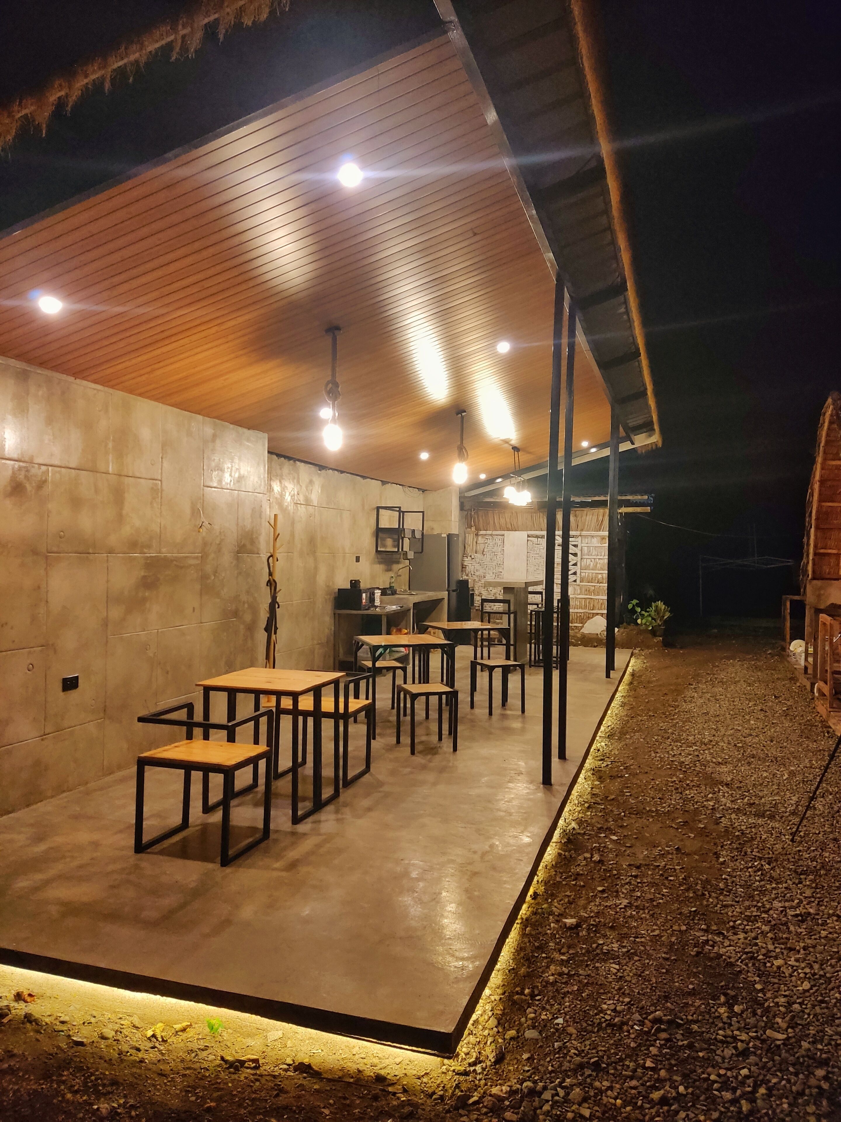 Un espacio interior amplio con mesas y sillas, una pared de hormigón y un techo de madera.