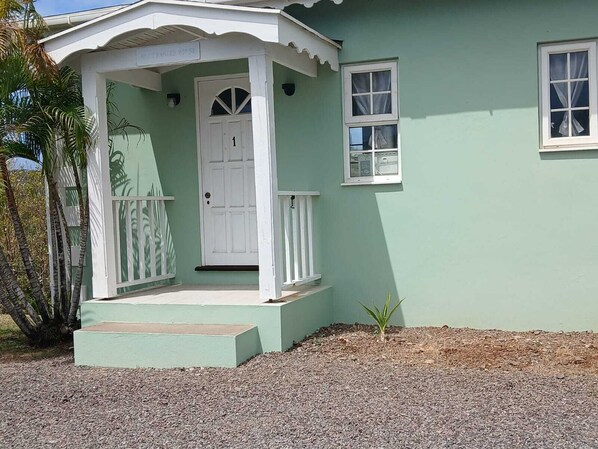 A house with a porch, a door marked with the number 1, and a small plant in the front yard.