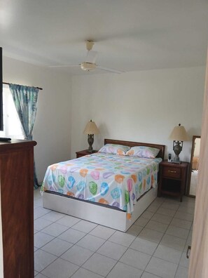 A bedroom with a bed, two bedside tables, a ceiling fan, and a window with curtains.