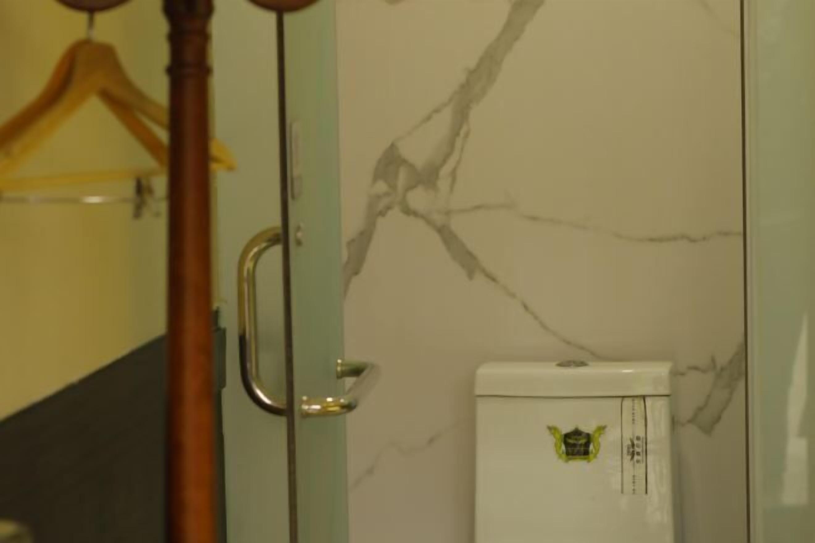 Un baño con pared de mármol, inodoro blanco y perchero de madera.