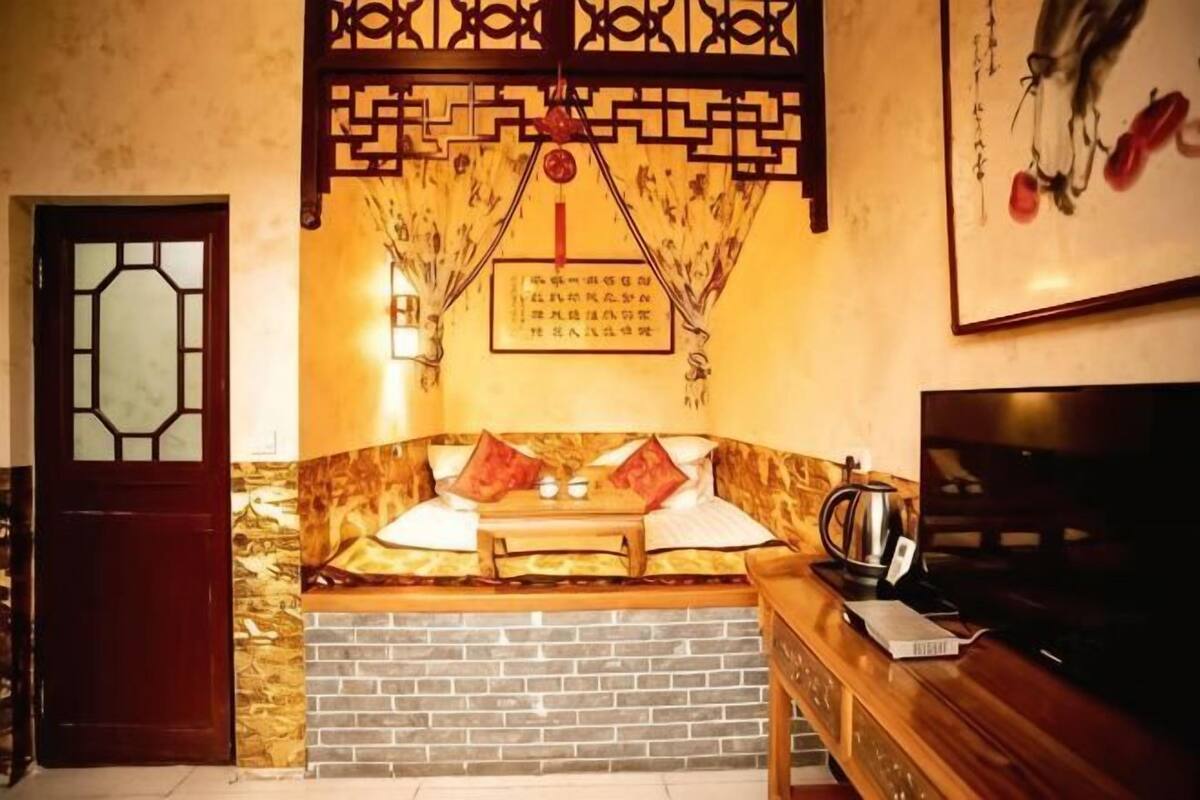 Una habitación tradicional con puerta de madera, un banco con cojines, pared de ladrillo y un cuadro enmarcado.