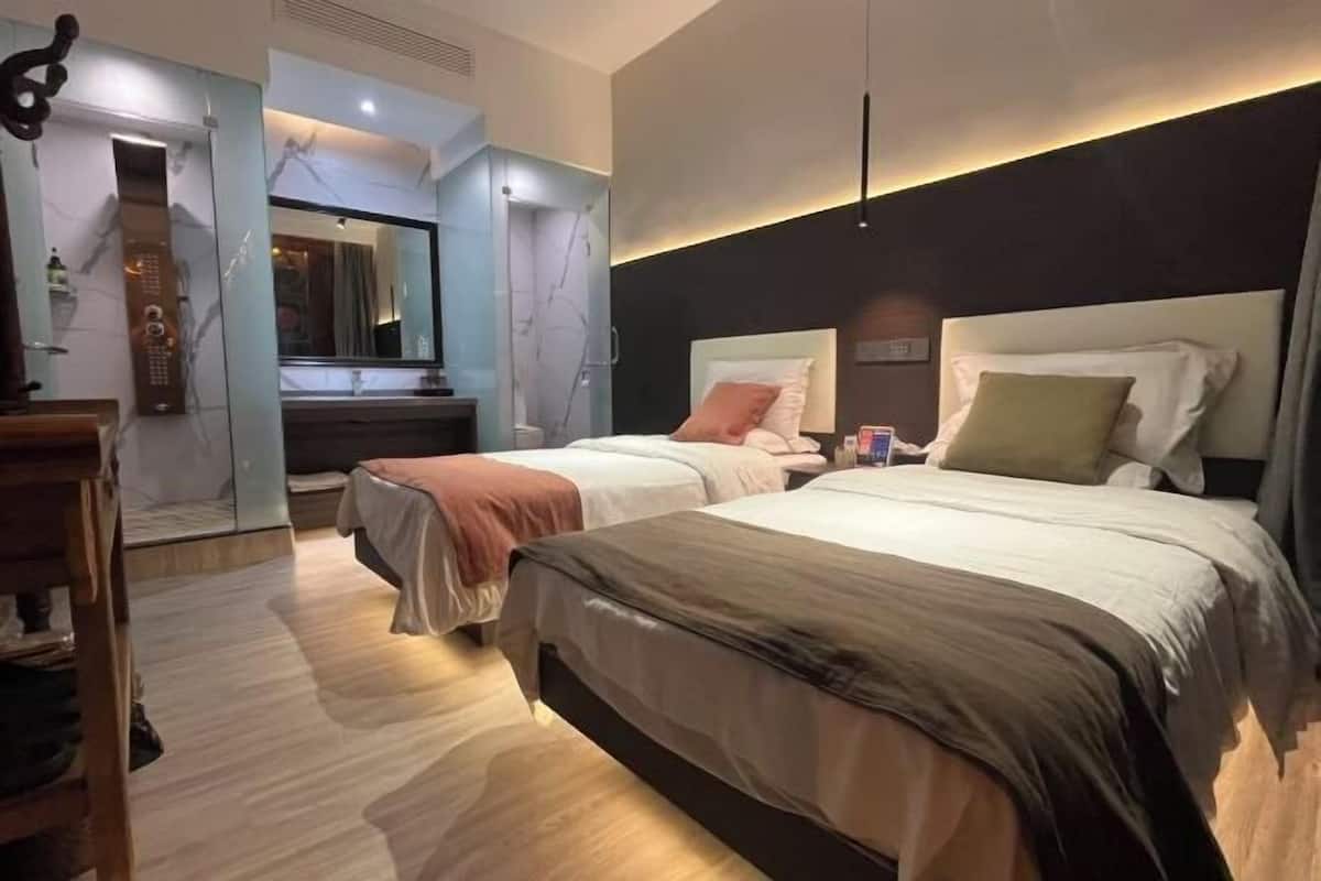Habitación de hotel con dos camas, un espejo, un aparador de madera y una lámpara moderna.