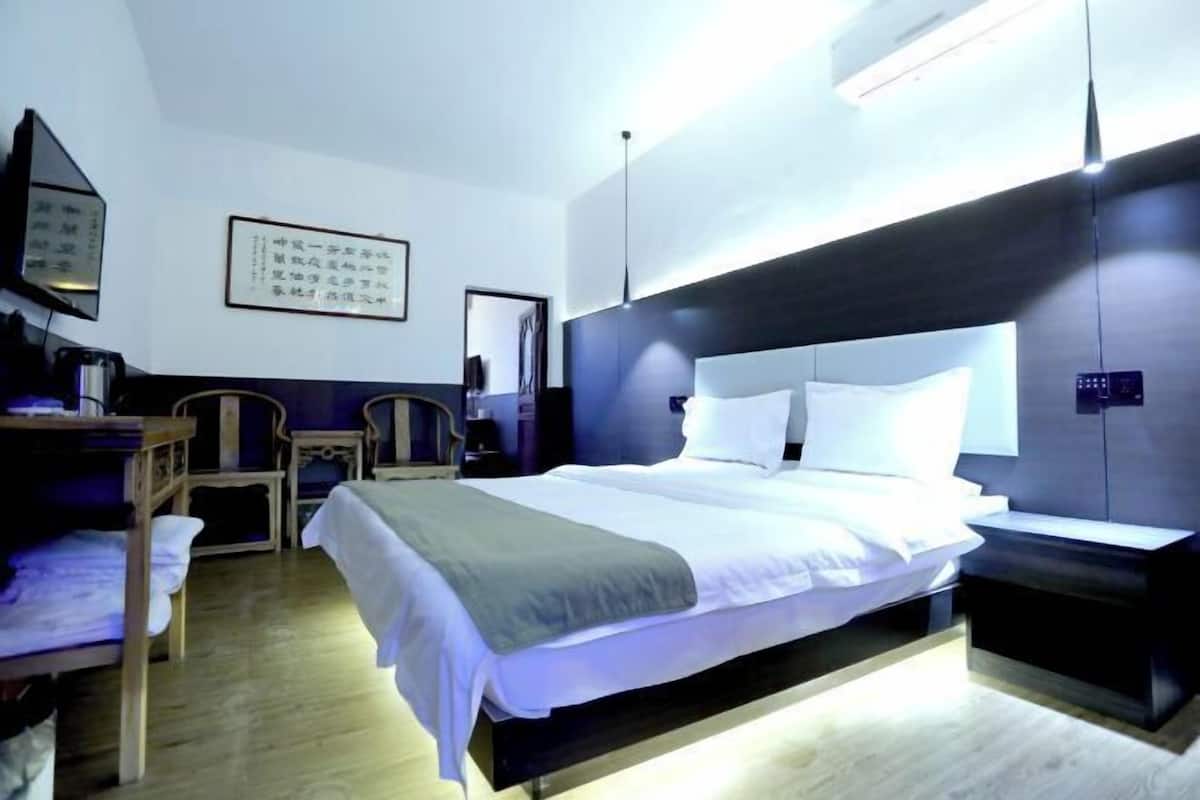 Habitación de hotel con cama, mesita de noche, silla y televisor instalado en la pared.