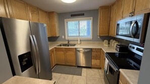 A kitchen with wooden cabinets, stainless steel appliances, a dishwasher, and a window with blinds. - C 23 Sundown Condominiums (Pensacola)