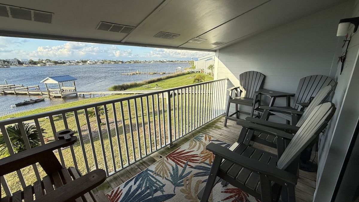 A balcony with a view of a body of water, dock, and chairs.