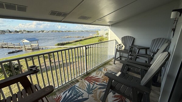 A balcony with a view of a body of water, dock, and chairs.