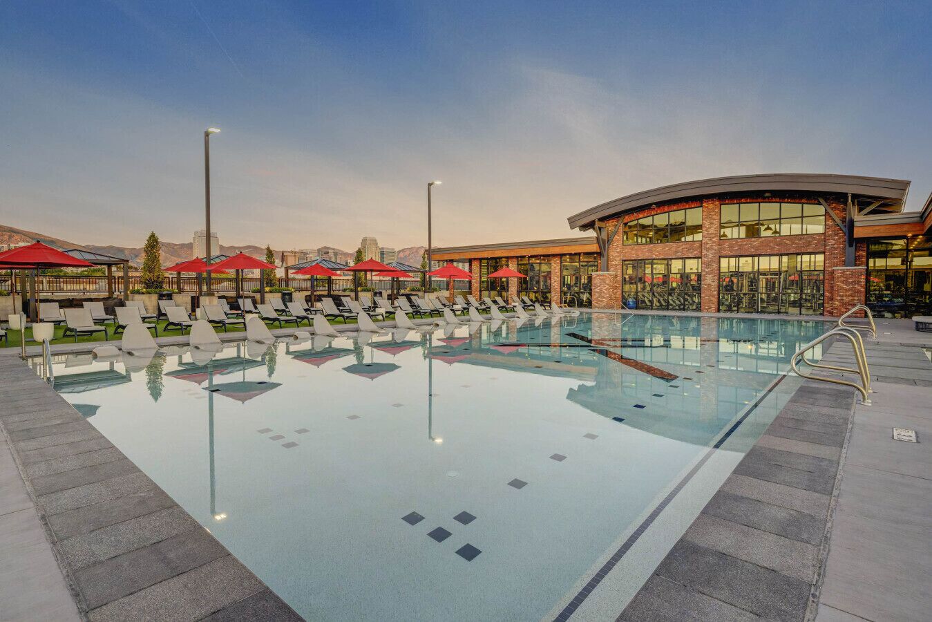 A swimming pool with lounge chairs and umbrellas, surrounded by a building with large windows and a curved roof.