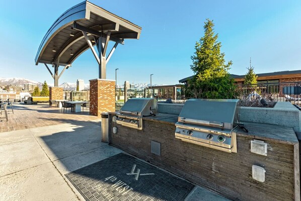 An outdoor patio with a grill and seating area, a covered structure, and a view of mountains in the background.