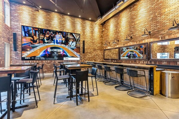 Un bar deportivo con varias televisiones mostrando partidos de baloncesto, taburetes de bar y paredes interiores de ladrillo.