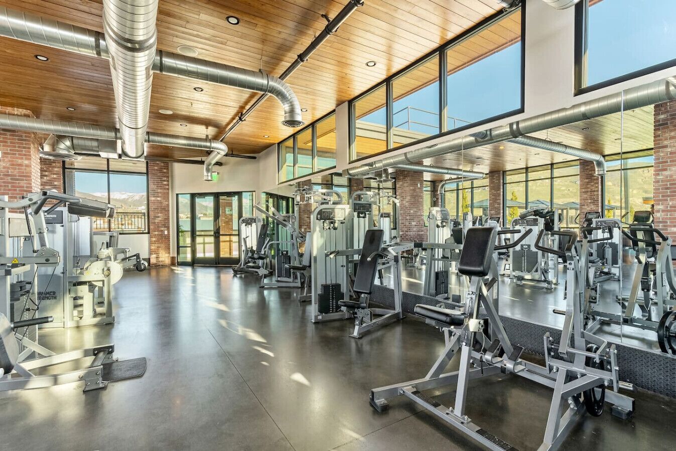 Une salle de sport équipée de divers appareils d’exercice, dotée de grandes fenêtres et d’un plafond en bois.