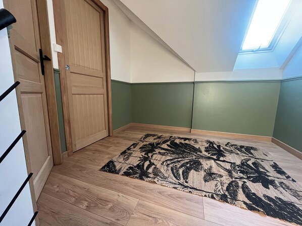 Una habitación con piso de madera, un tapete estampado, una puerta y un tragaluz.