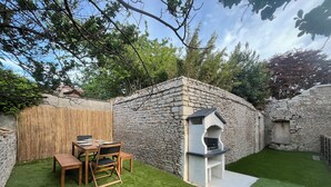 A stone wall, a wooden table with chairs, and a barbecue grill in a backyard. - Welcome to la Nacrière - House Bourg de Mer - 3 Bedrooms and more (Courseulles-sur-Mer)
