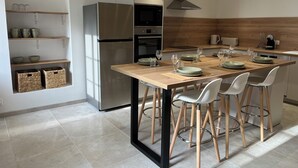 A modern kitchen with a central island, built-in appliances, and a dining area with chairs and table set for four. - Welcome to la Nacrière - House Bourg de Mer - 3 Bedrooms and more (Courseulles-sur-Mer)