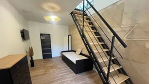 A modern bedroom with a wooden floor, a bed with a black frame, a dresser, a bookshelf, and a staircase with a black railing. - Welcome to la Nacrière - House Bourg de Mer - 3 Bedrooms and more (Courseulles-sur-Mer)