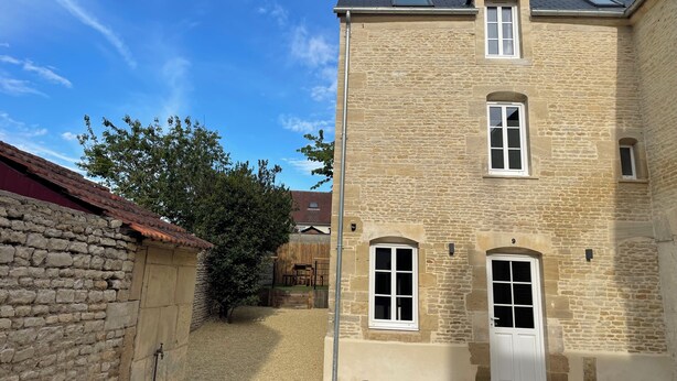 A two-story stone building with a gravel driveway, a small garden, and a red-roofed structure to the left. - Welcome to la Nacrière - House Bourg de Mer - 3 Bedrooms and more (Courseulles-sur-Mer)