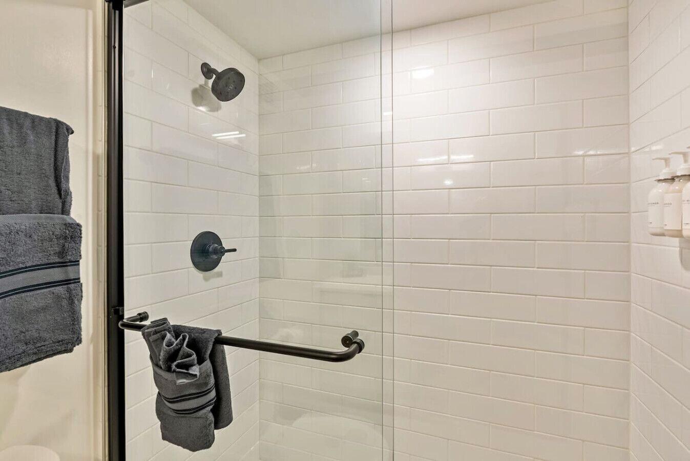 A modern bathroom with white subway tiles, a glass shower enclosure, and a towel rack with towels.