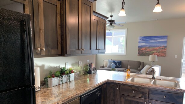 A kitchen with dark wooden cabinets, a granite countertop, a built-in dishwasher, and a window with a view of the outdoors. - Luxury Townhouse in the Heart of Southern Utah (Cedar City)