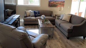 A living room with a sofa, a coffee table, a TV, and a painting on the wall. - Luxury Townhouse in the Heart of Southern Utah (Cedar City)