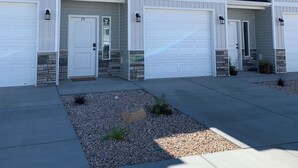A row of two-story houses with white exteriors and grey roofs, featuring multiple garage doors and a small landscaped area in front. - Luxury Townhouse in the Heart of Southern Utah (Cedar City)