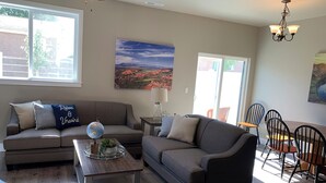 A modern living room with a gray sofa, a wooden coffee table, and a dining area with black chairs. - Luxury Townhouse in the Heart of Southern Utah (Cedar City)