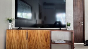 A flat-screen TV on a wooden cabinet with a small shelf below. - Loft in La Veleta w/ Pool,Balcony and rooftop! Near beach cenotes downtown (Q.R.)