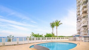 Una piscina con valla blanca, palmeras y vista al océano.