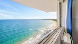 Vista desde una ventana sobre una playa con agua azul cristalina y una orilla arenosa.