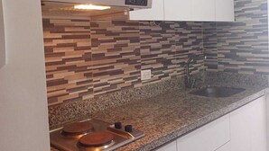 A kitchen with white cabinets, a granite countertop, a built-in stove, and a patterned backsplash. - Modern loft  Bogotá international center (Bogotá)