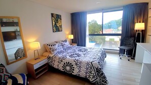 A hotel room with a bed, two bedside lamps, a desk with a chair, a large window with curtains, and a mirror on the wall. - Modern loft  Bogotá international center (Bogotá)