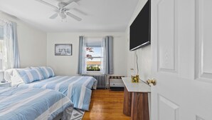 A bedroom with two beds, a ceiling fan, a window with curtains, a radiator, and a TV mounted on the wall.