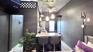 A modern kitchen with a bar area, a potted plant, and a seating area with a purple cushion.