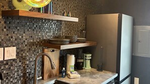 A modern kitchen with a sink, dishwasher, and a refrigerator. There are hanging pendant lights and a mosaic backsplash.