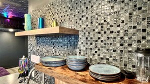 A kitchen with a wooden countertop, a sink, and a backsplash made of small, square tiles. There are several plates stacked on the counter.