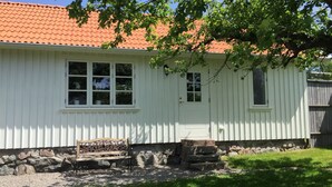 A white building with a red-tiled roof, a front door, and a bench outside.