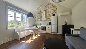A compact kitchen with white appliances, a dining area with a bench, and a grey sofa.